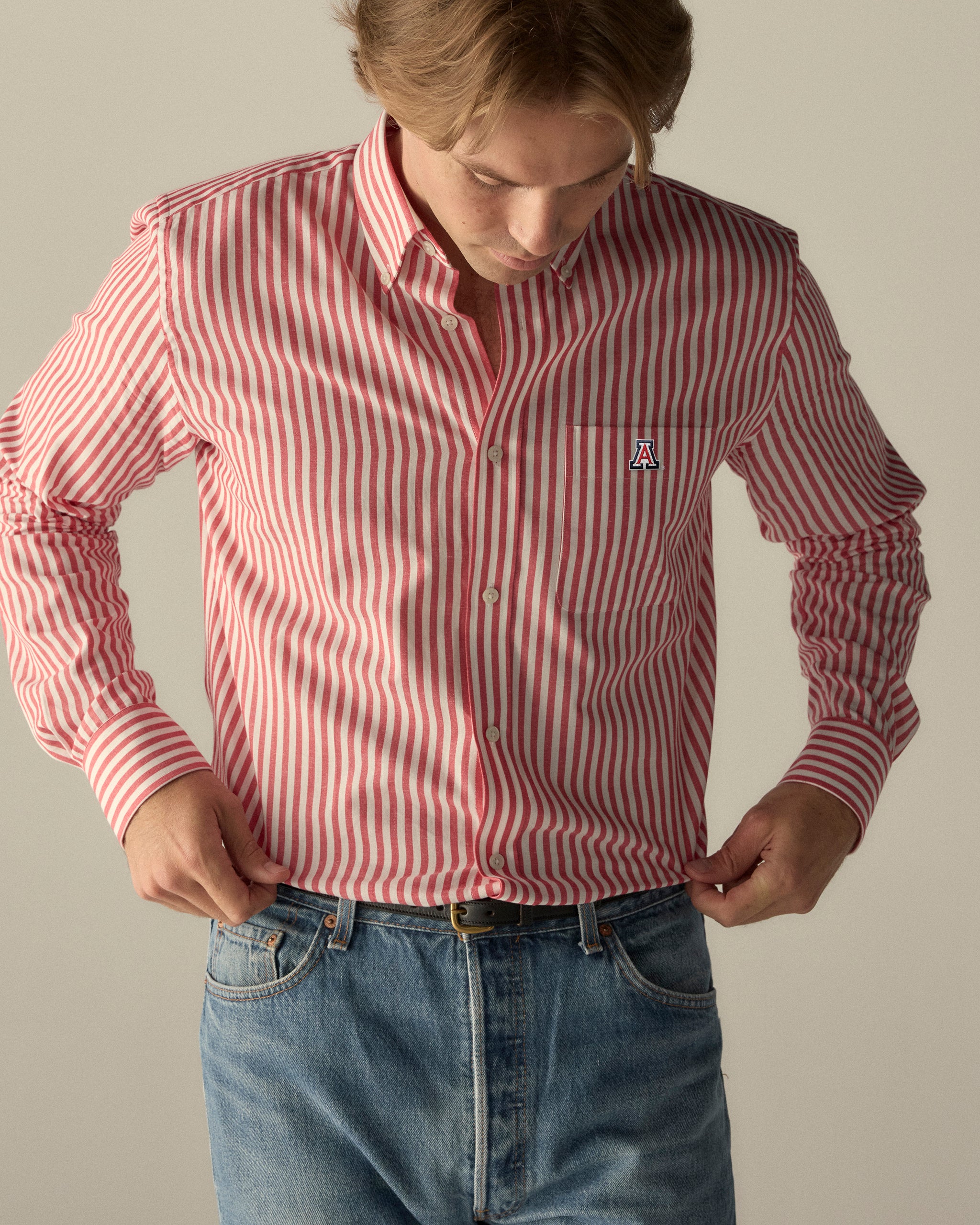 Man wearing red and white striped button-down shirt with Arizona 'A' logo, paired with jeans. Class Trip | Officially Licensed Collegiate Apparel