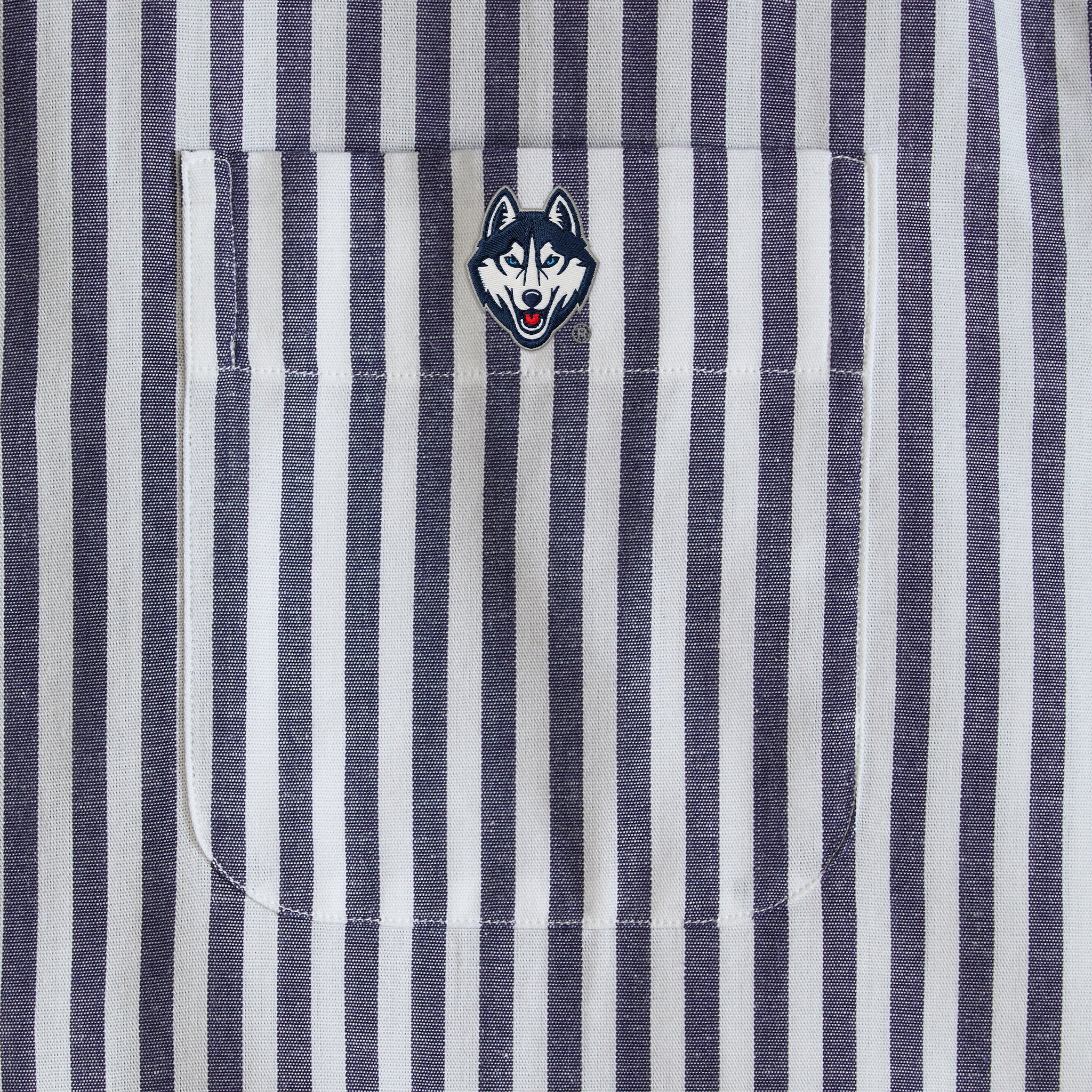 Navy and white striped shirt pocket with embroidered husky mascot patch detail. Class Trip | Officially Licensed Collegiate Apparel