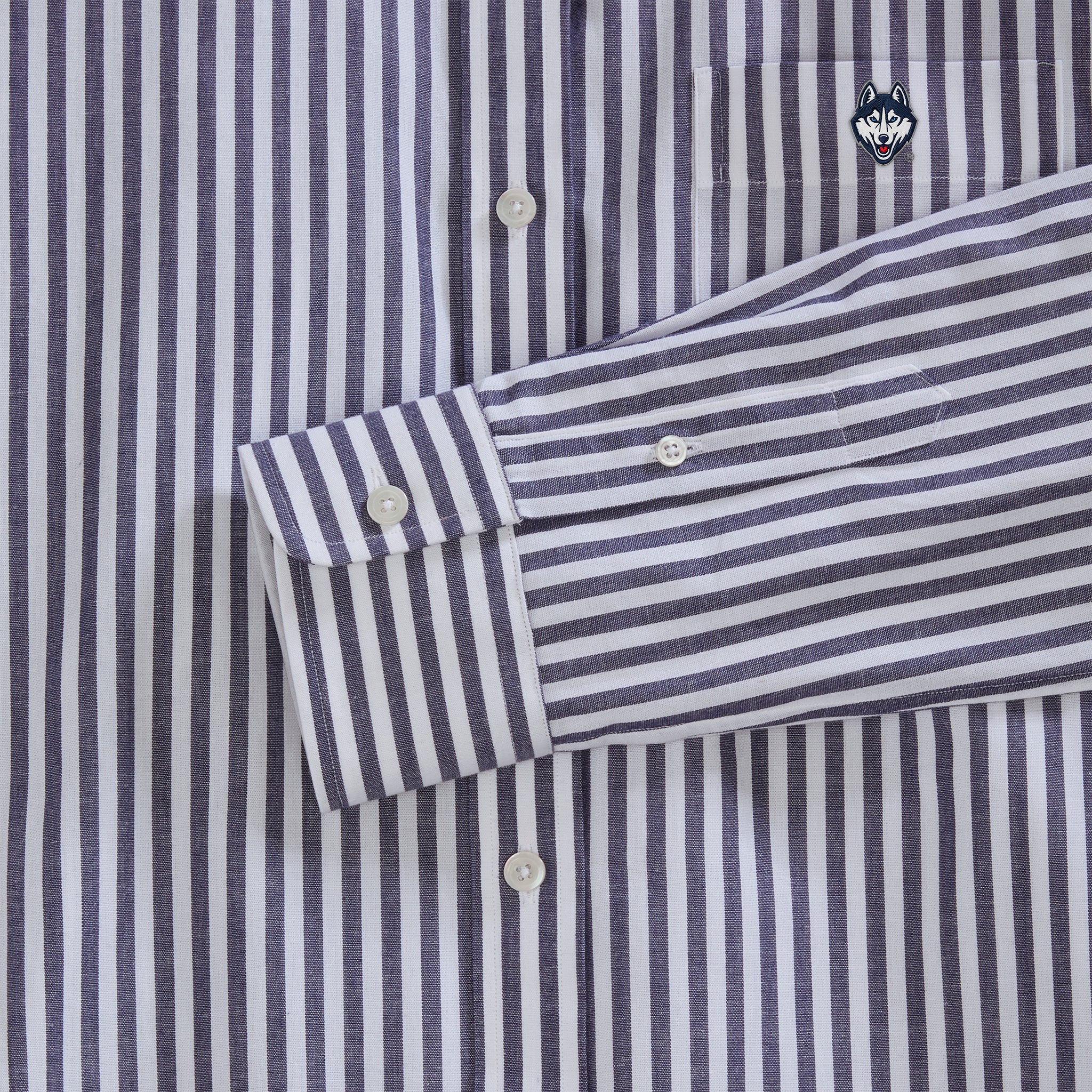 Close-up of navy striped poplin shirt with embroidered husky logo on pocket, white buttons. Class Trip | Officially Licensed Collegiate Apparel
