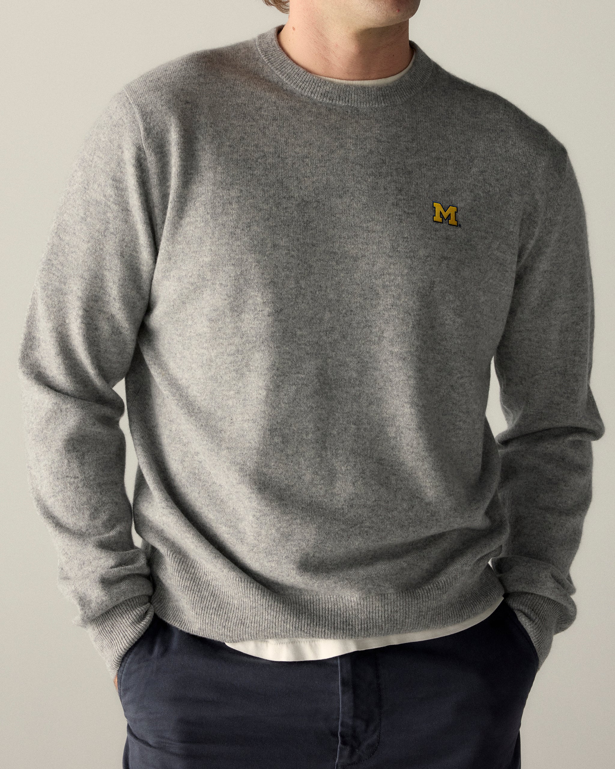 Man wearing grey collegiate crewneck sweater with yellow M logo, casual style. Class Trip | Officially Licensed Collegiate Apparel