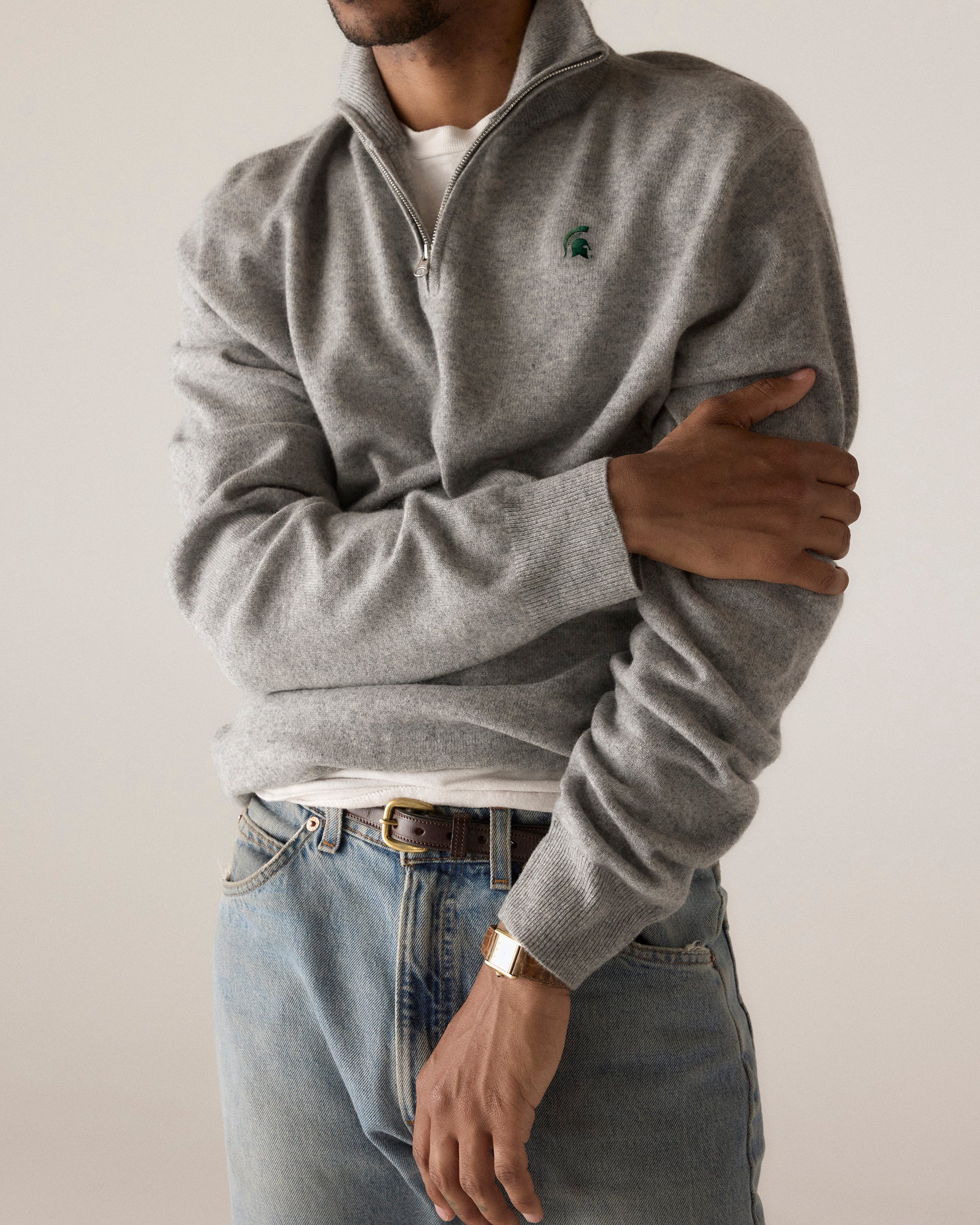 Man wearing grey collegiate quarter zip sweater with embroidered logo, blue jeans, gold watch. Class Trip | Officially Licensed Collegiate Apparel