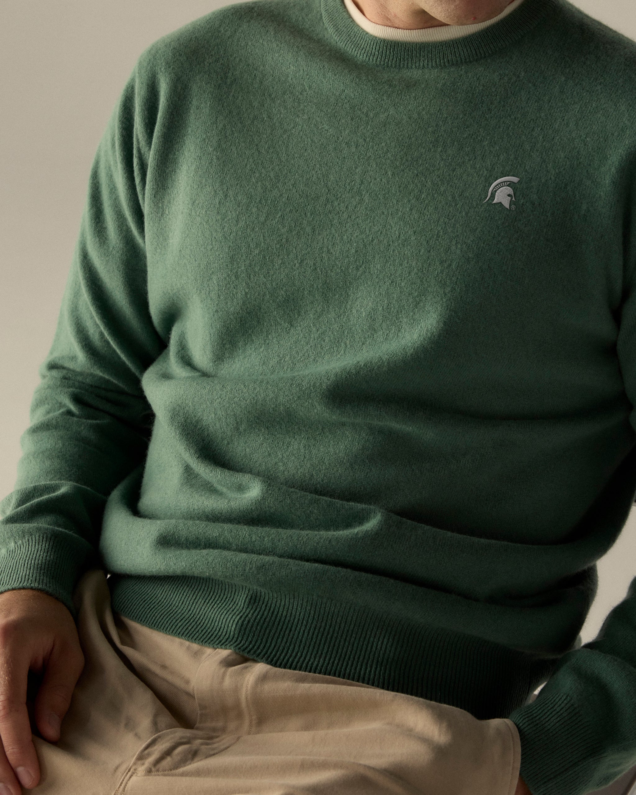 Men's green merino crewneck sweater with collegiate logo, beige pants. Class Trip | Officially Licensed Collegiate Apparel