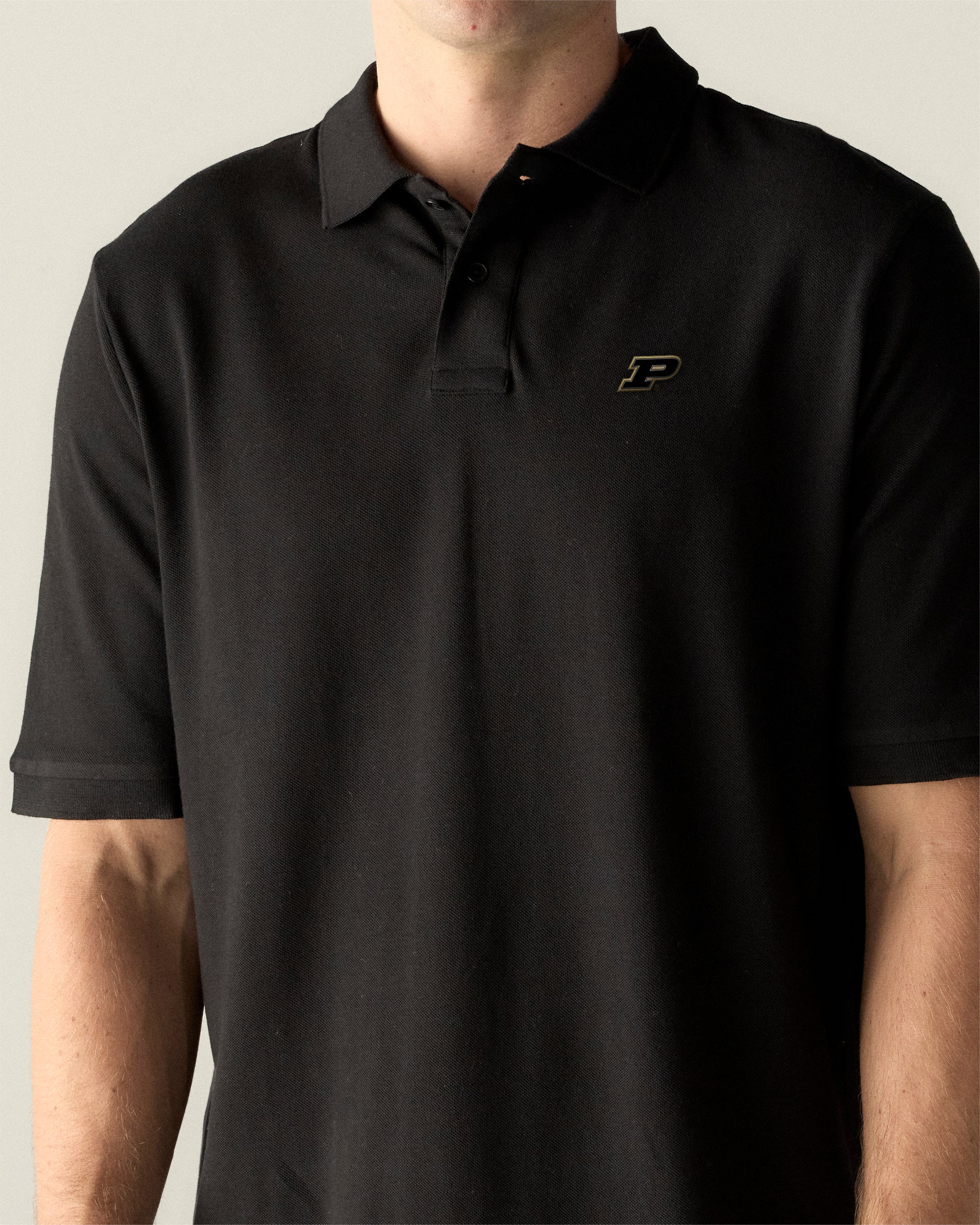 Black pique polo shirt with embroidered collegiate logo on chest, worn by male model. Class Trip | Officially Licensed Collegiate Apparel