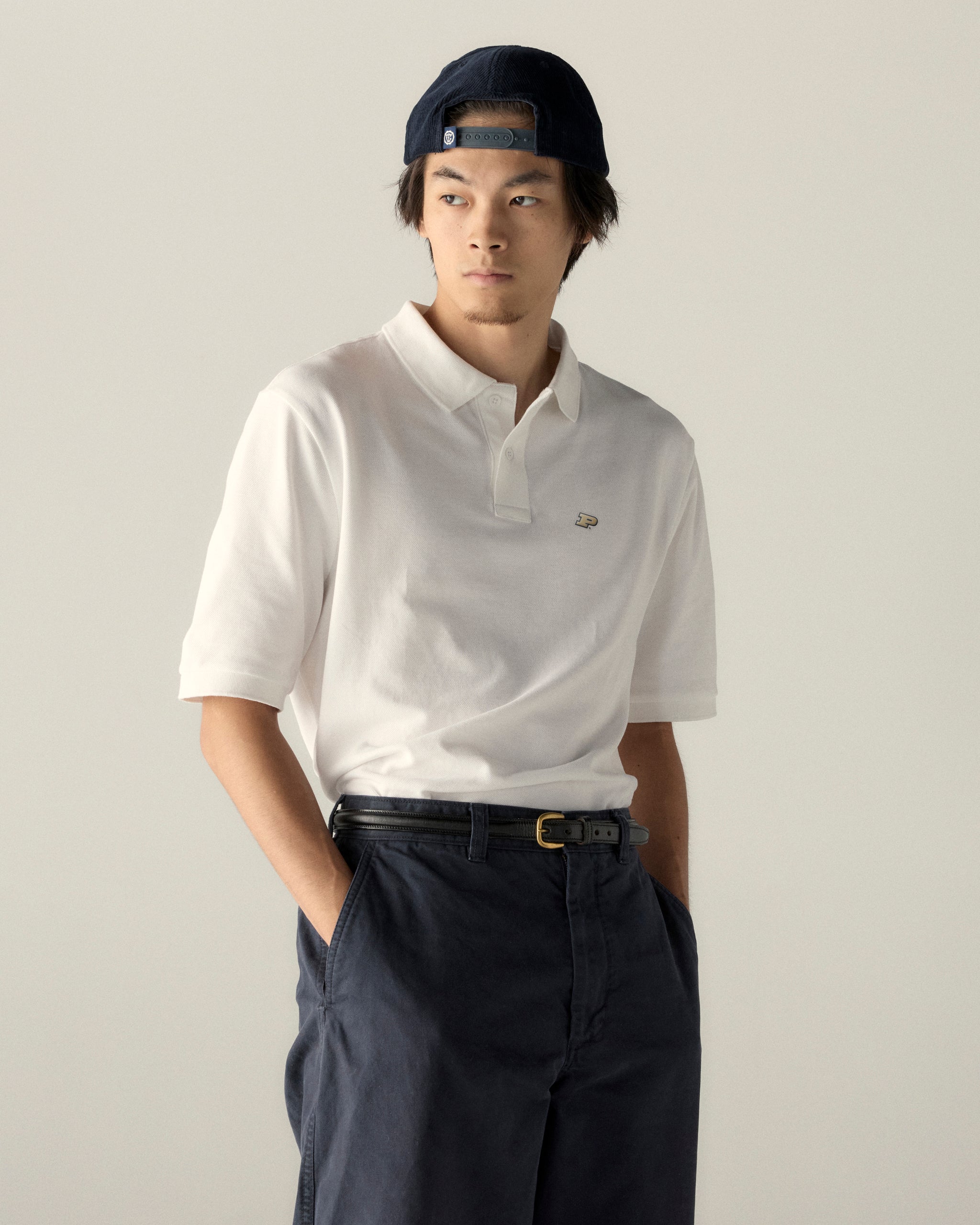 Man in white collegiate polo shirt and navy cap, casual outfit. Class Trip | Officially Licensed Collegiate Apparel