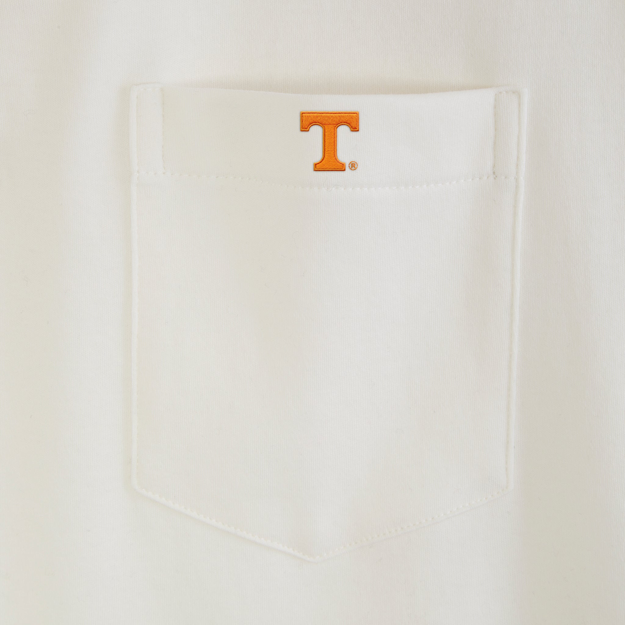White polo shirt pocket with orange collegiate T logo embroidery. Class Trip | Officially Licensed Collegiate Apparel