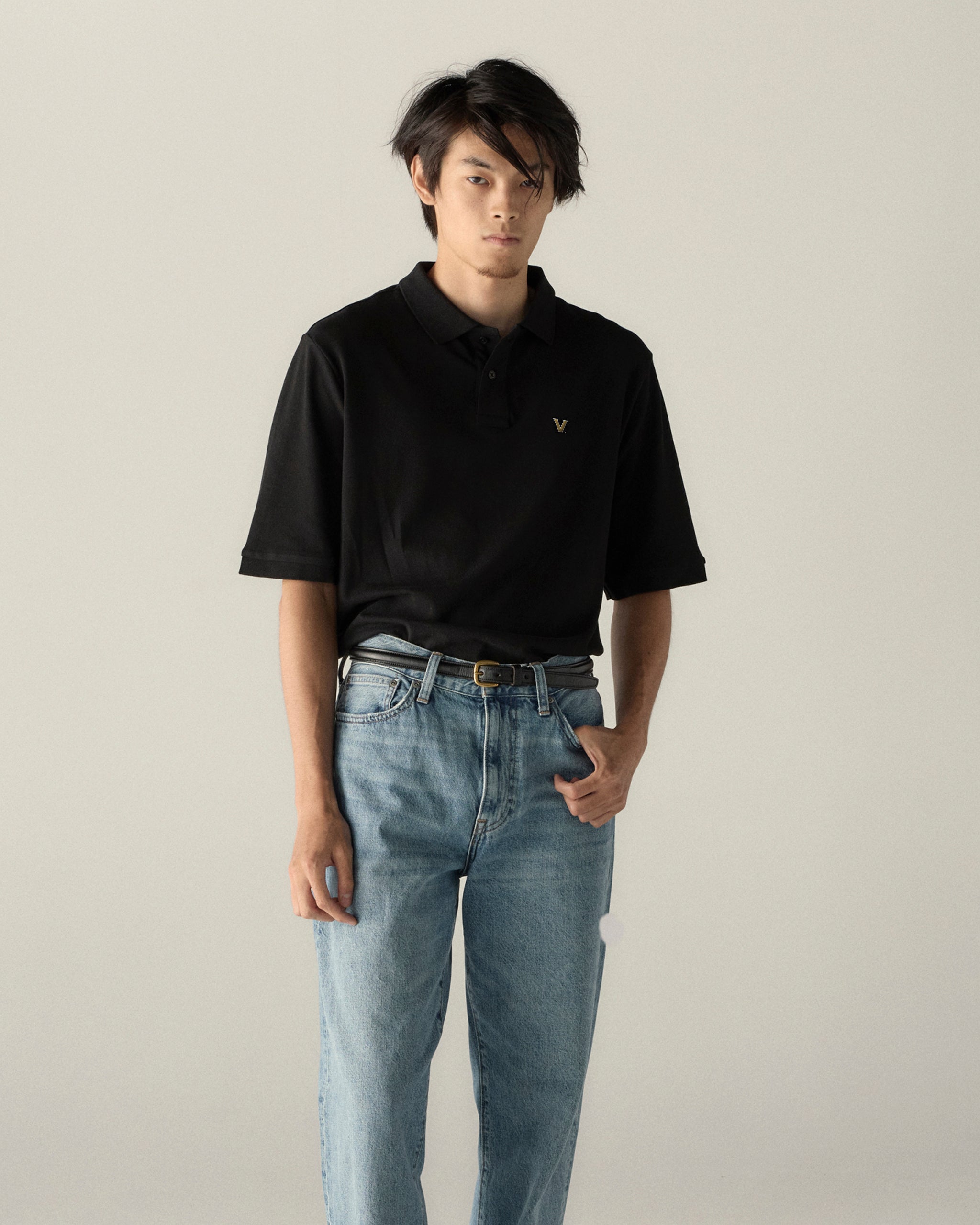 Man in black pique polo shirt with gold emblem and blue jeans, collegiate style. Class Trip | Officially Licensed Collegiate Apparel