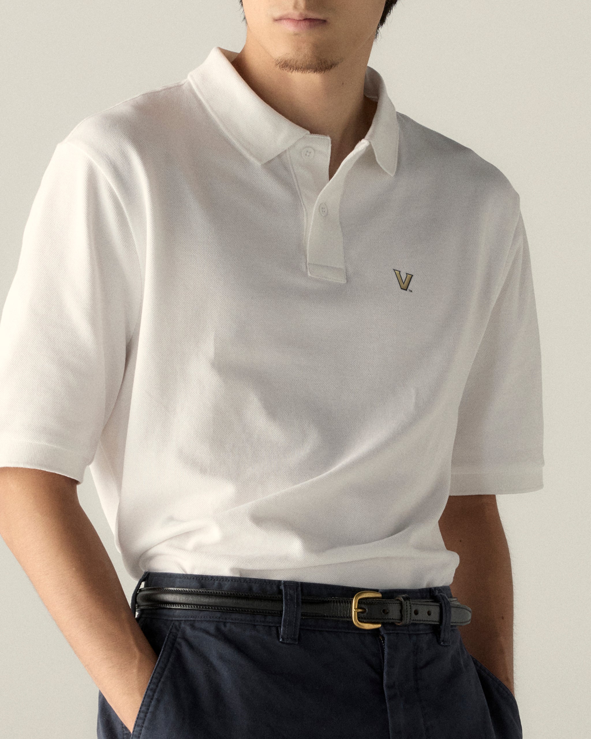 White collegiate polo shirt with V logo, paired with dark pants. Class Trip | Officially Licensed Collegiate Apparel