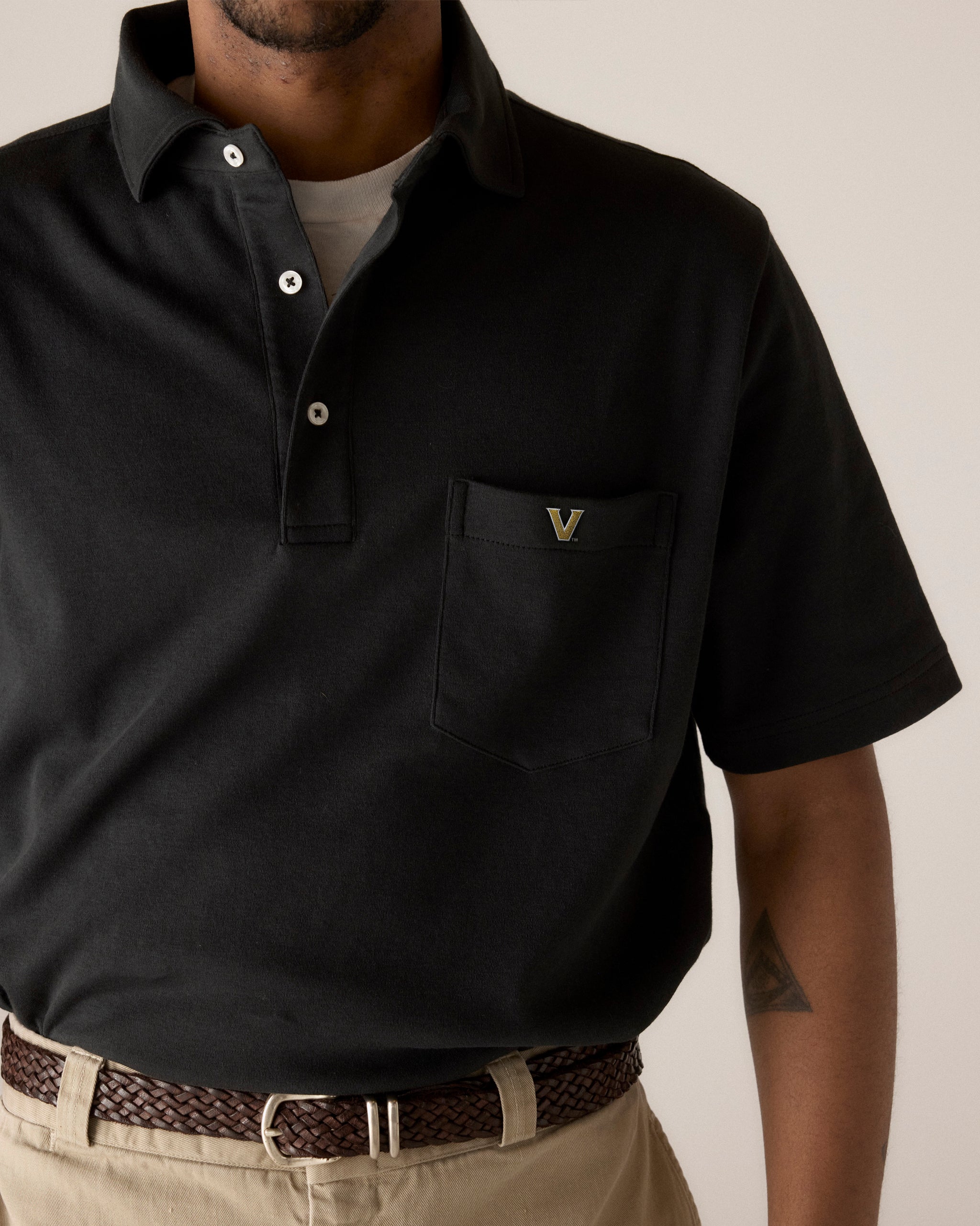 Black collegiate polo shirt with V logo on pocket, styled with khaki pants. Class Trip | Officially Licensed Collegiate Apparel