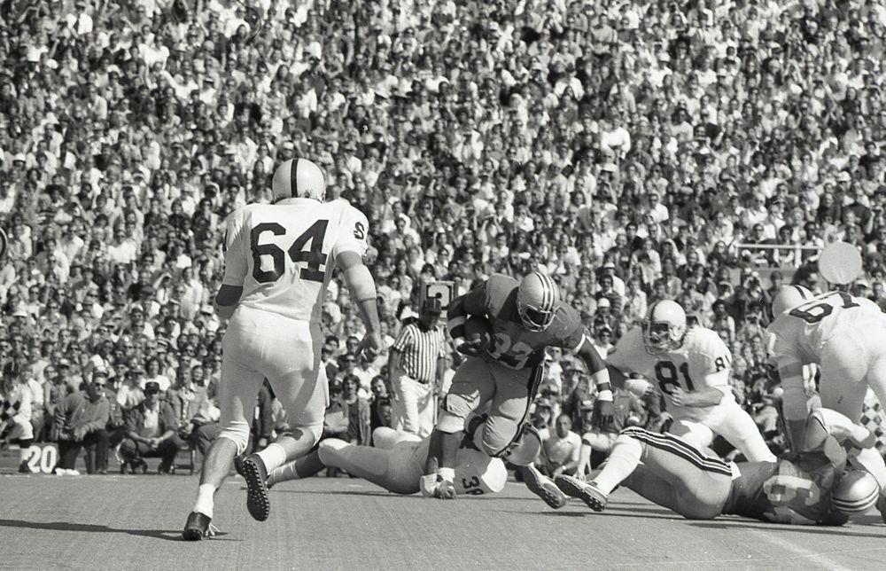 Vintage college football game with players in action, crowded stadium background. Class Trip | Officially Licensed Collegiate Apparel