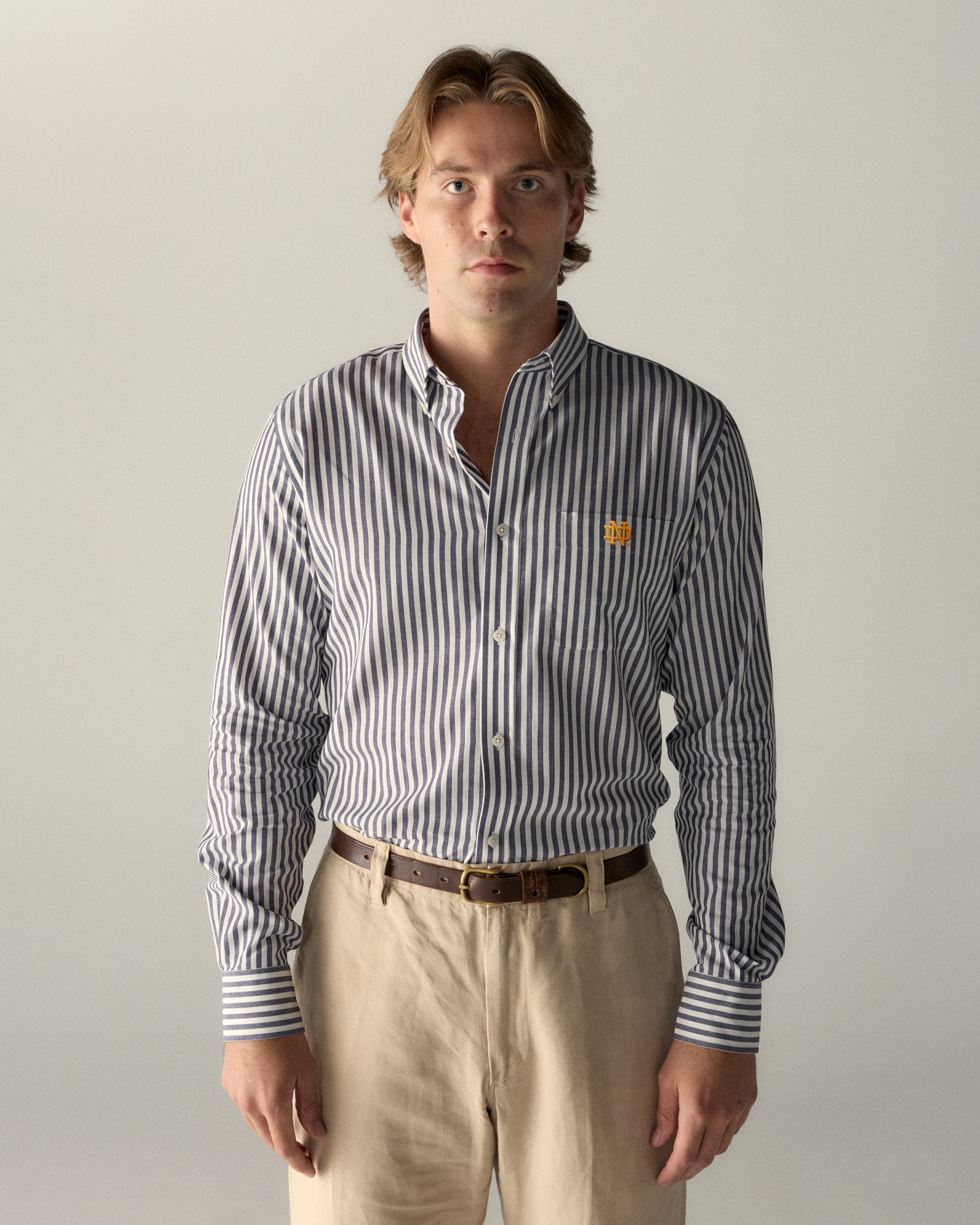 Man in blue and white striped collegiate button-down shirt with logo and beige pants, Class Trip | Officially Licensed Collegiate Apparel