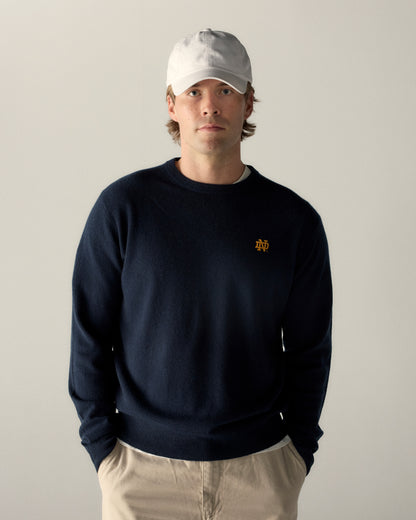 Man in navy merino crewneck sweater with gold collegiate logo, beige hat and pants. Class Trip | Officially Licensed Collegiate Apparel