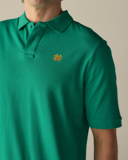 Green polo shirt with gold collegiate embroidery on chest, short sleeves. Class Trip | Officially Licensed Collegiate Apparel