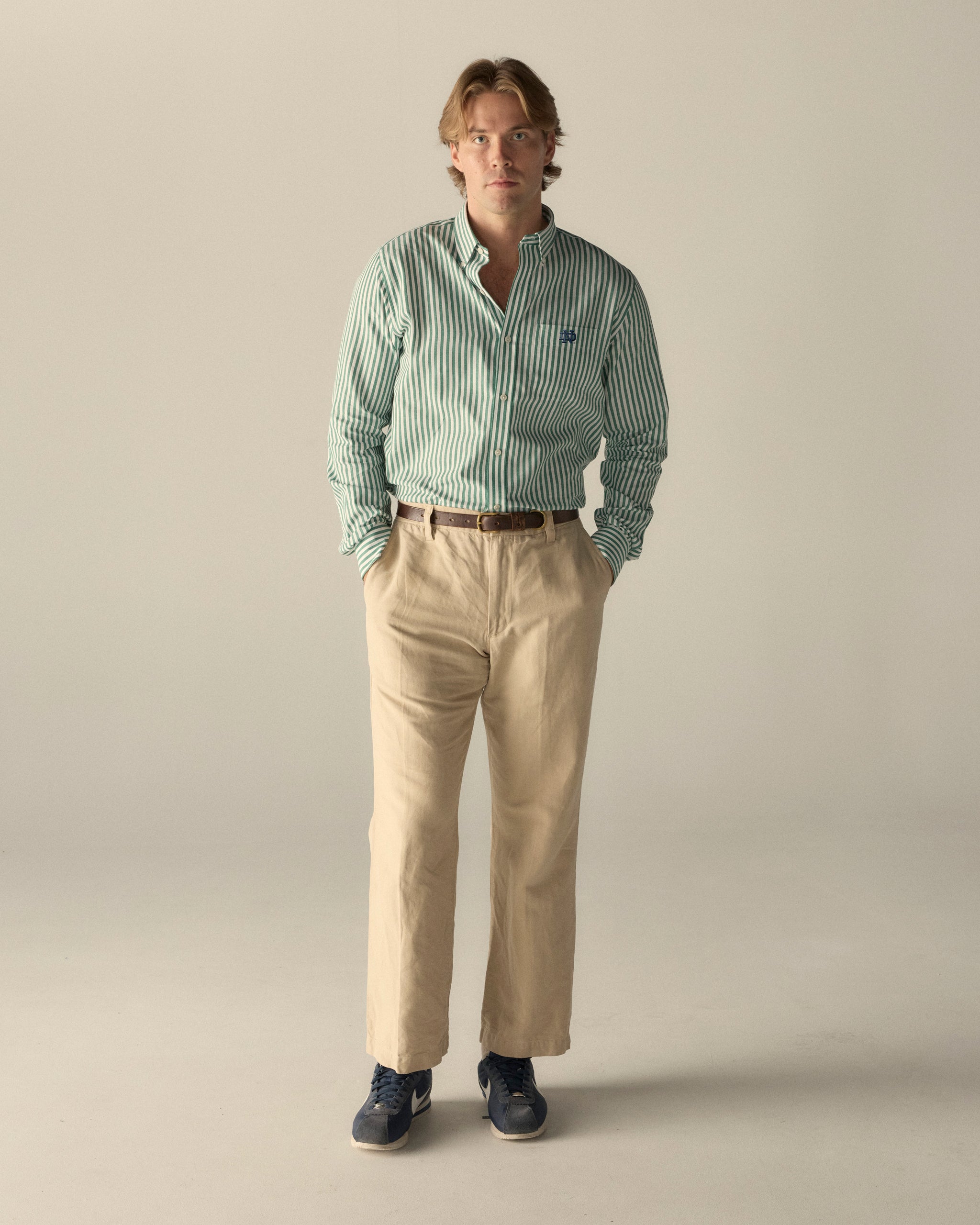 Man wearing green striped poplin shirt and beige chinos, collegiate style. Class Trip | Officially Licensed Collegiate Apparel