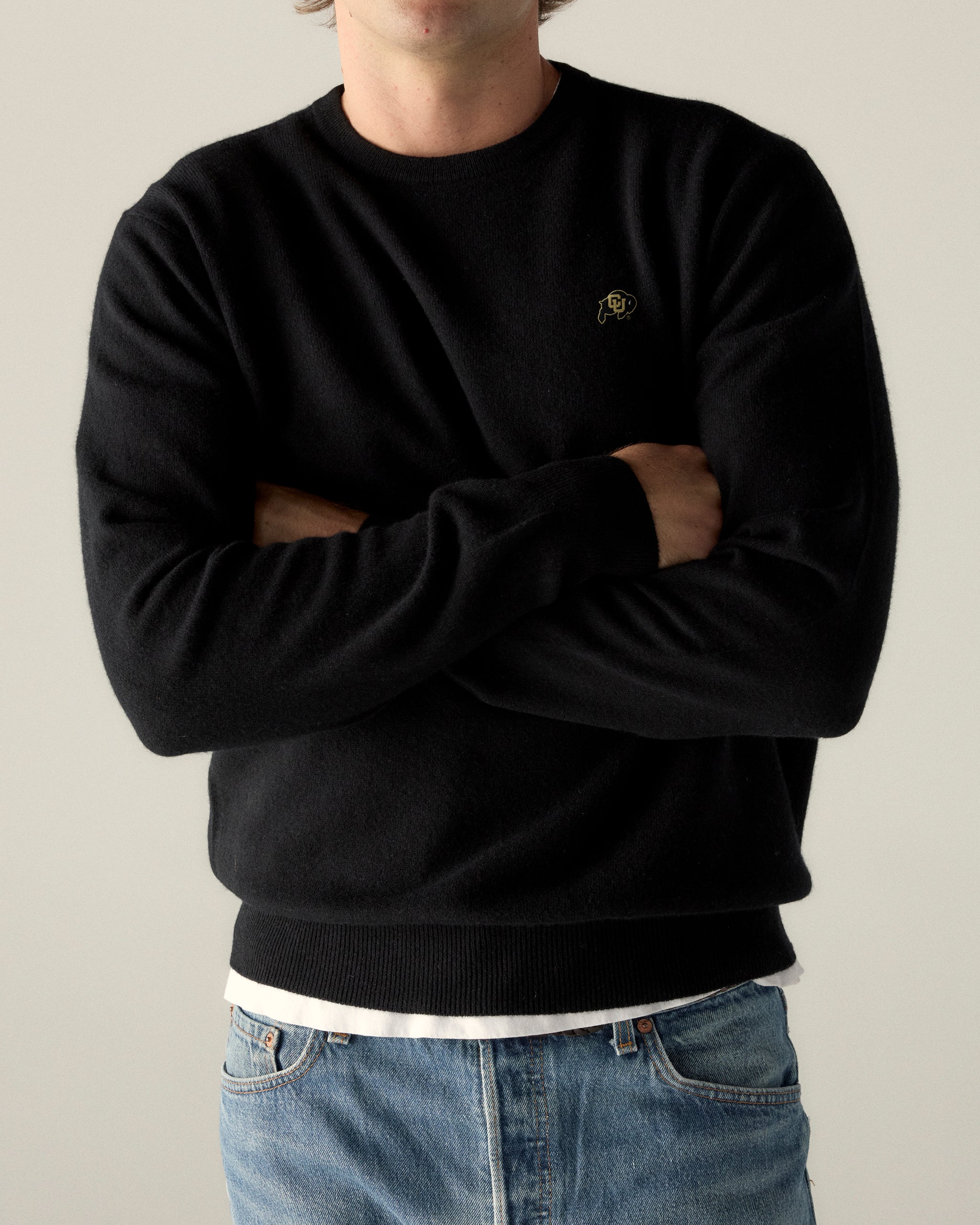 Man wearing black merino crewneck sweater with university logo and blue jeans. Class Trip | Officially Licensed Collegiate Apparel