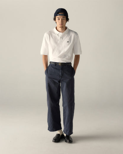 Man wearing a white pique polo shirt, navy pants, black loafers, and a backwards cap, standing against a plain background. Class Trip | Officially Licensed Collegiate Apparel