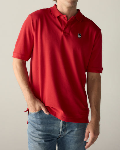 Red collegiate polo shirt with wolf emblem, paired with blue jeans. Class Trip | Officially Licensed Collegiate Apparel