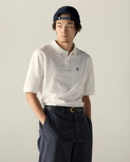 Man wearing white collegiate polo shirt and navy cap, official campus apparel. Class Trip | Officially Licensed Collegiate Apparel