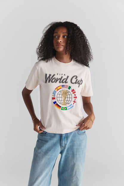 Cream FIFA World Cup graphic tee with global flags and trophy design, paired with denim. World Cup Tee | Class Trip | Higher Education