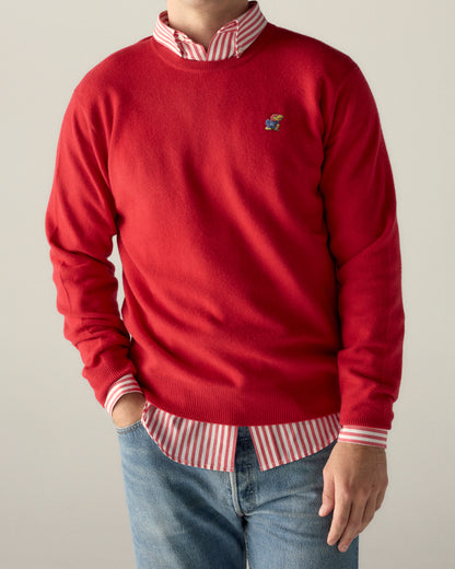 Red crewneck sweater with KU Jayhawk logo, layered over striped button-down shirt, paired with jeans. Class Trip | Officially Licensed Collegiate Apparel