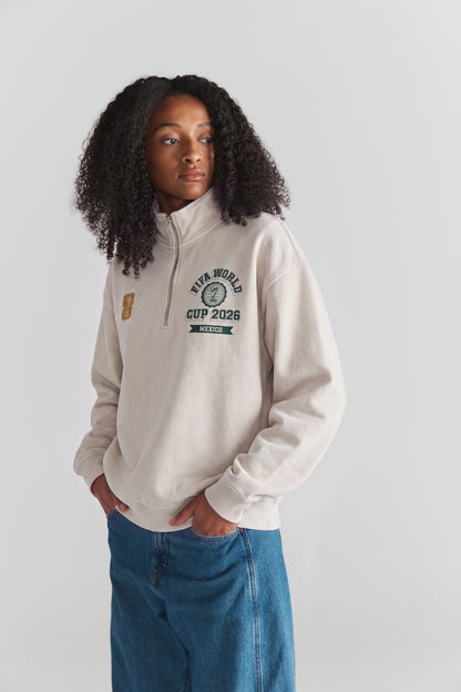 Cream half-zip sweatshirt with FIFA World Cup 2026 Mexico graphic, worn with blue jeans. Class Trip | Higher Education