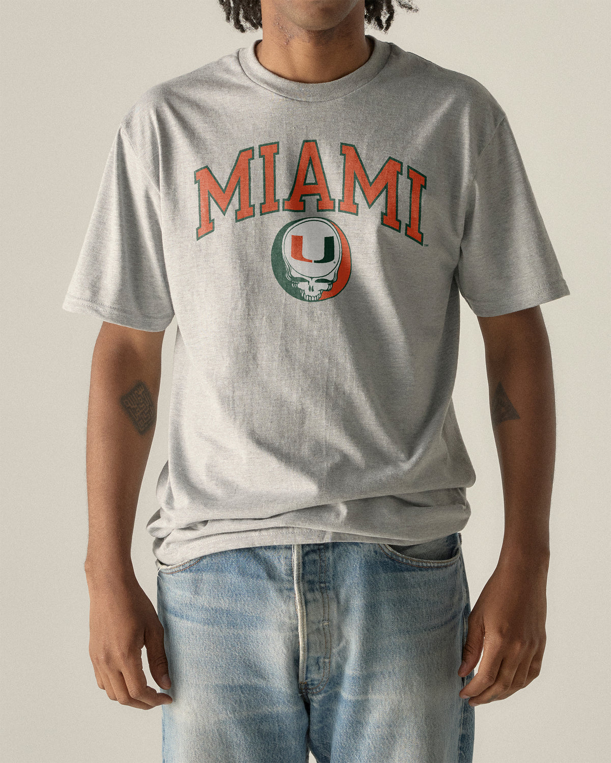 Man wearing a grey University of Miami x Grateful Dead Steal Your Face Arch Tee. Class Trip | Higher Education