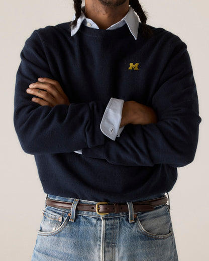 Man wearing navy merino sweater with yellow M logo over collared shirt and jeans. Class Trip | Officially Licensed Collegiate Apparel
