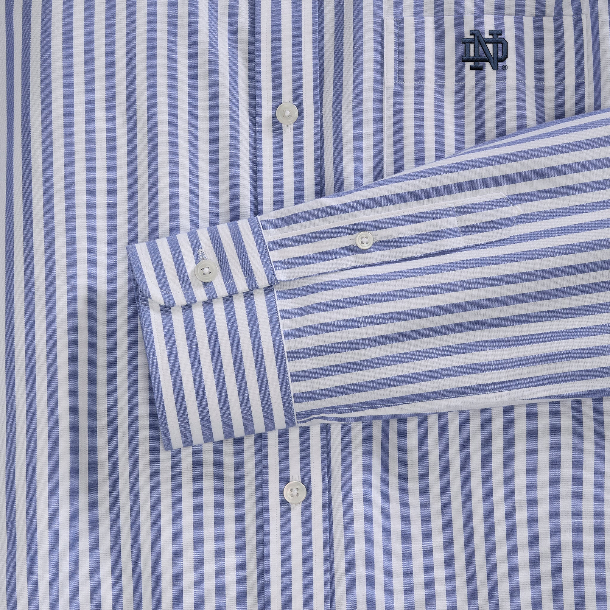 Close-up of blue and white striped women's poplin shirt with embroidered collegiate logo, button details. Class Trip | Officially Licensed Collegiate Apparel