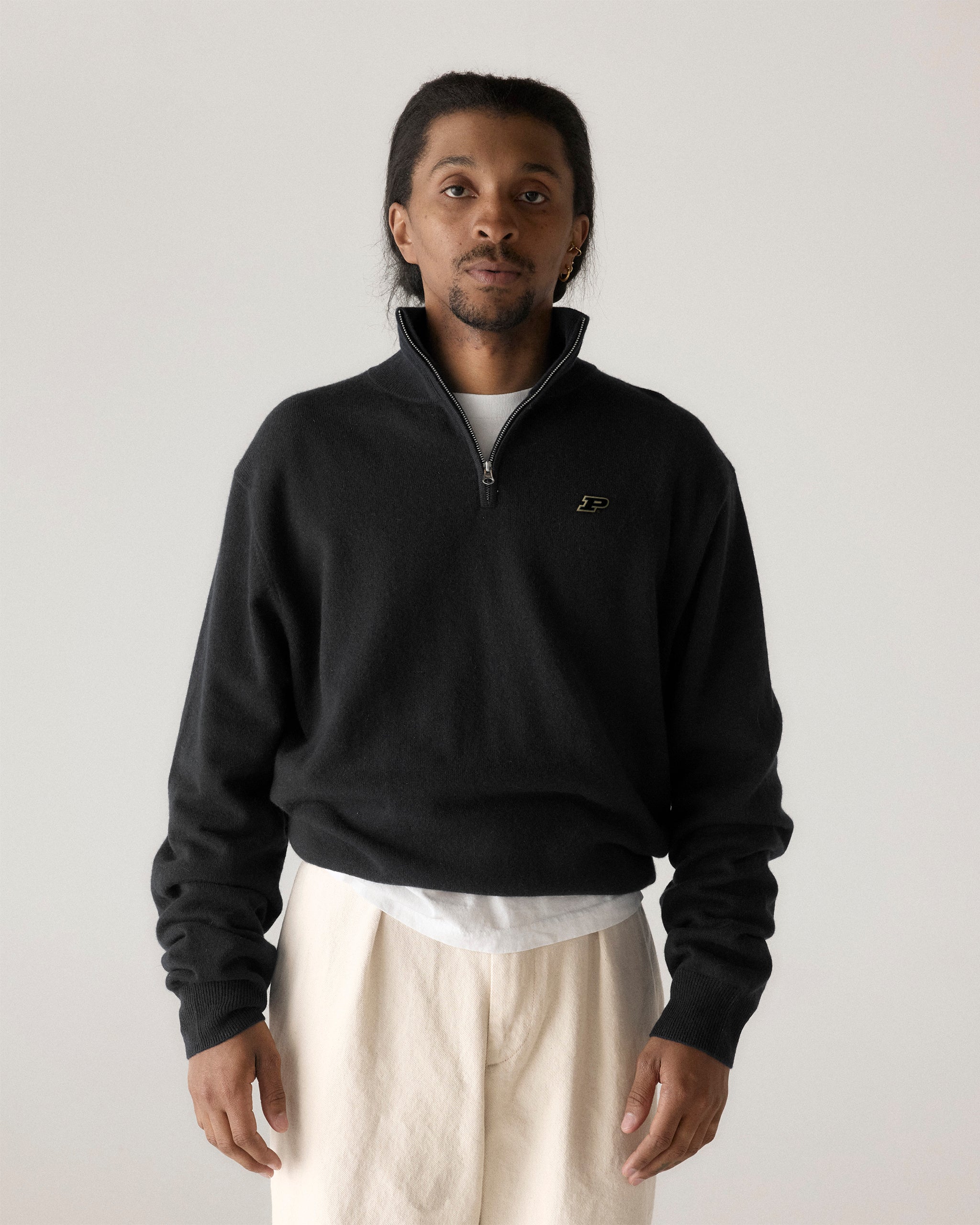 Man wearing a black collegiate quarter zip pullover with embroidered logo, light pants. Class Trip | Officially Licensed Collegiate Apparel