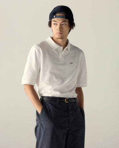 Man in white collegiate polo shirt and navy cap, casual outfit. Class Trip | Officially Licensed Collegiate Apparel