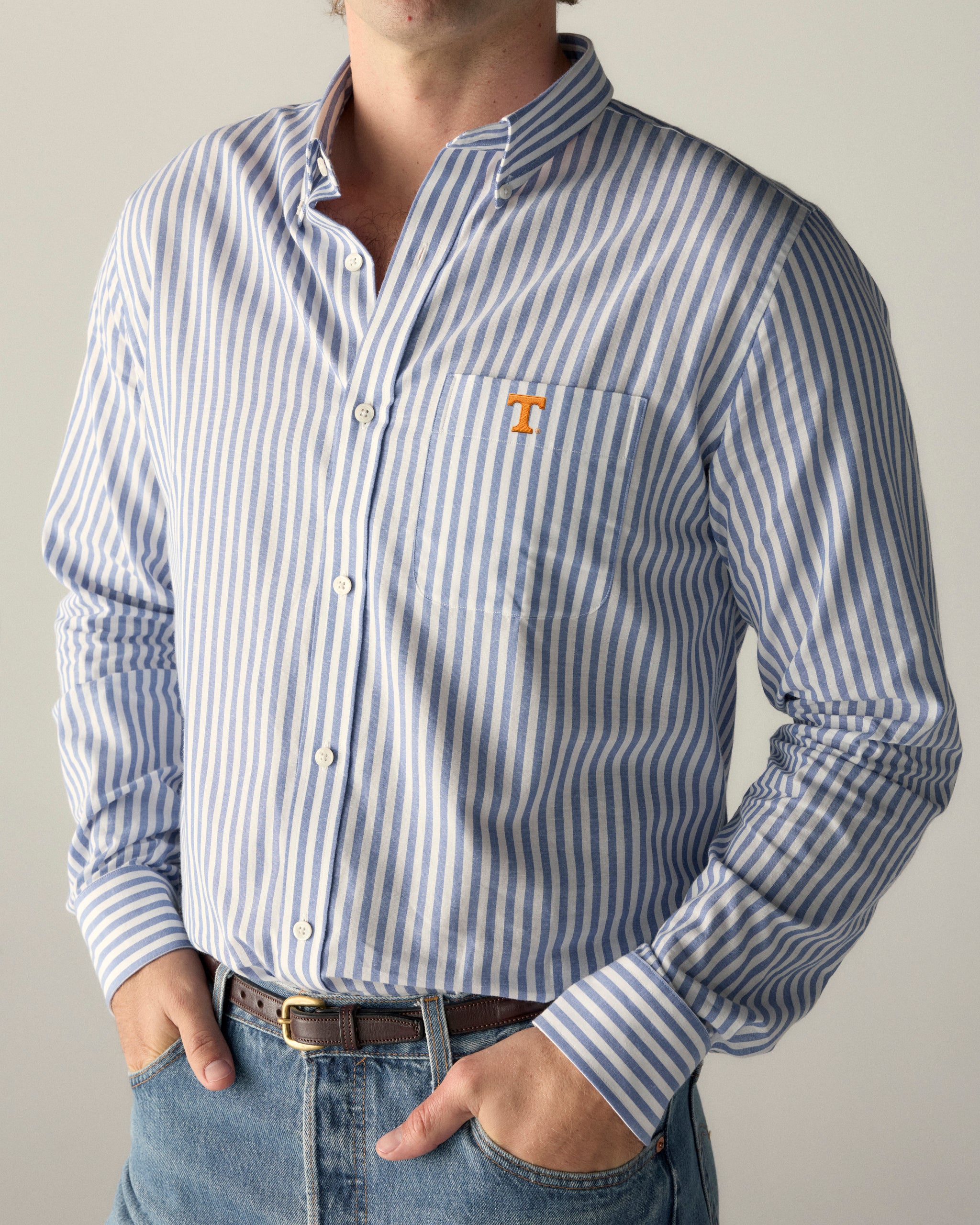Man wearing blue and white striped collegiate shirt with orange logo, hands in pockets. Class Trip | Officially Licensed Collegiate Apparel