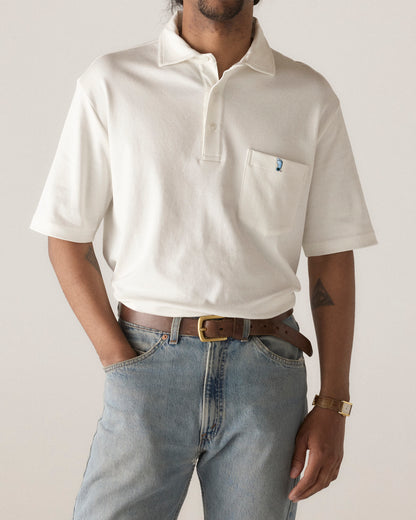 Cream polo shirt with foot logo, paired with light jeans and brown belt. Class Trip | Officially Licensed Collegiate Apparel