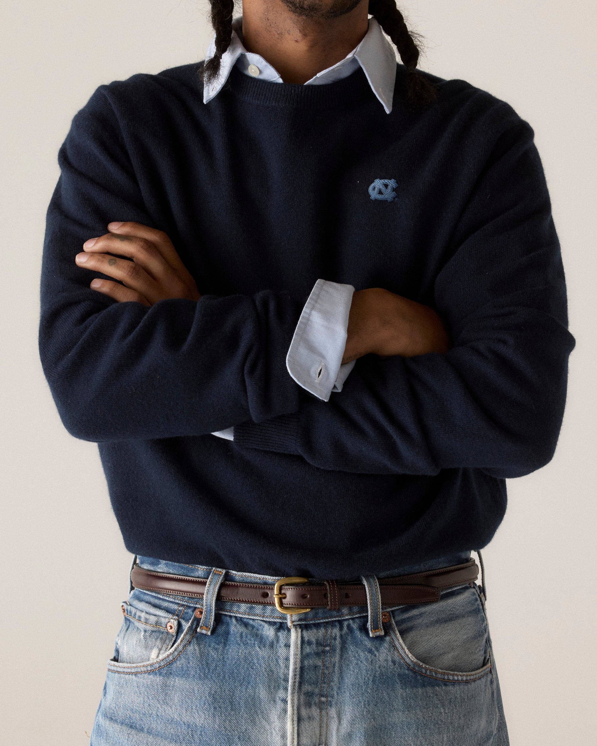 Man in navy UNC merino sweater with light blue shirt and jeans, arms crossed. Class Trip | Officially Licensed Collegiate Apparel
