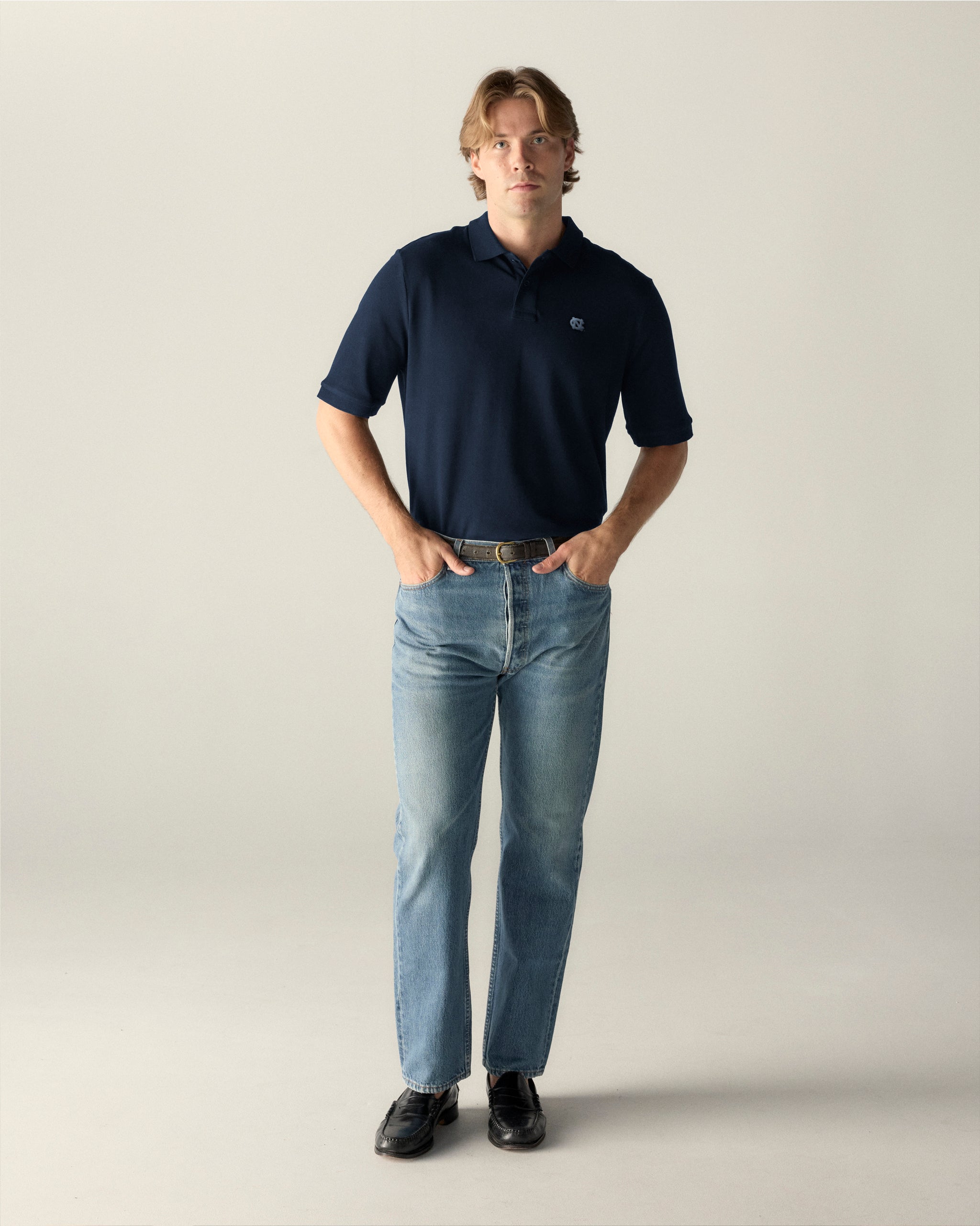 Navy blue UNC polo shirt with light blue logo, paired with jeans and loafers. Class Trip | Officially Licensed Collegiate Apparel