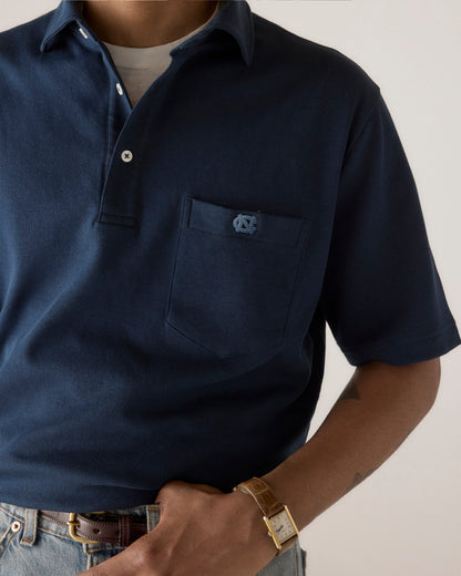Navy blue polo shirt with embroidered logo, paired with jeans and a watch. Class Trip | Officially Licensed Collegiate Apparel