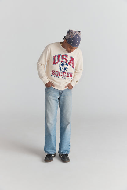 Cream USA Soccer sweatshirt with FIFA World Cup 2026 graphic, worn with jeans and bandana. Class Trip | Higher Education