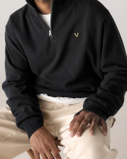 Man wearing black quarter zip sweater with V logo and cream pants, casual collegiate style. Class Trip | Officially Licensed Collegiate Apparel