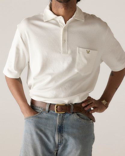 White collegiate pocket polo shirt with V logo, styled with jeans and brown belt. Class Trip | Officially Licensed Collegiate Apparel